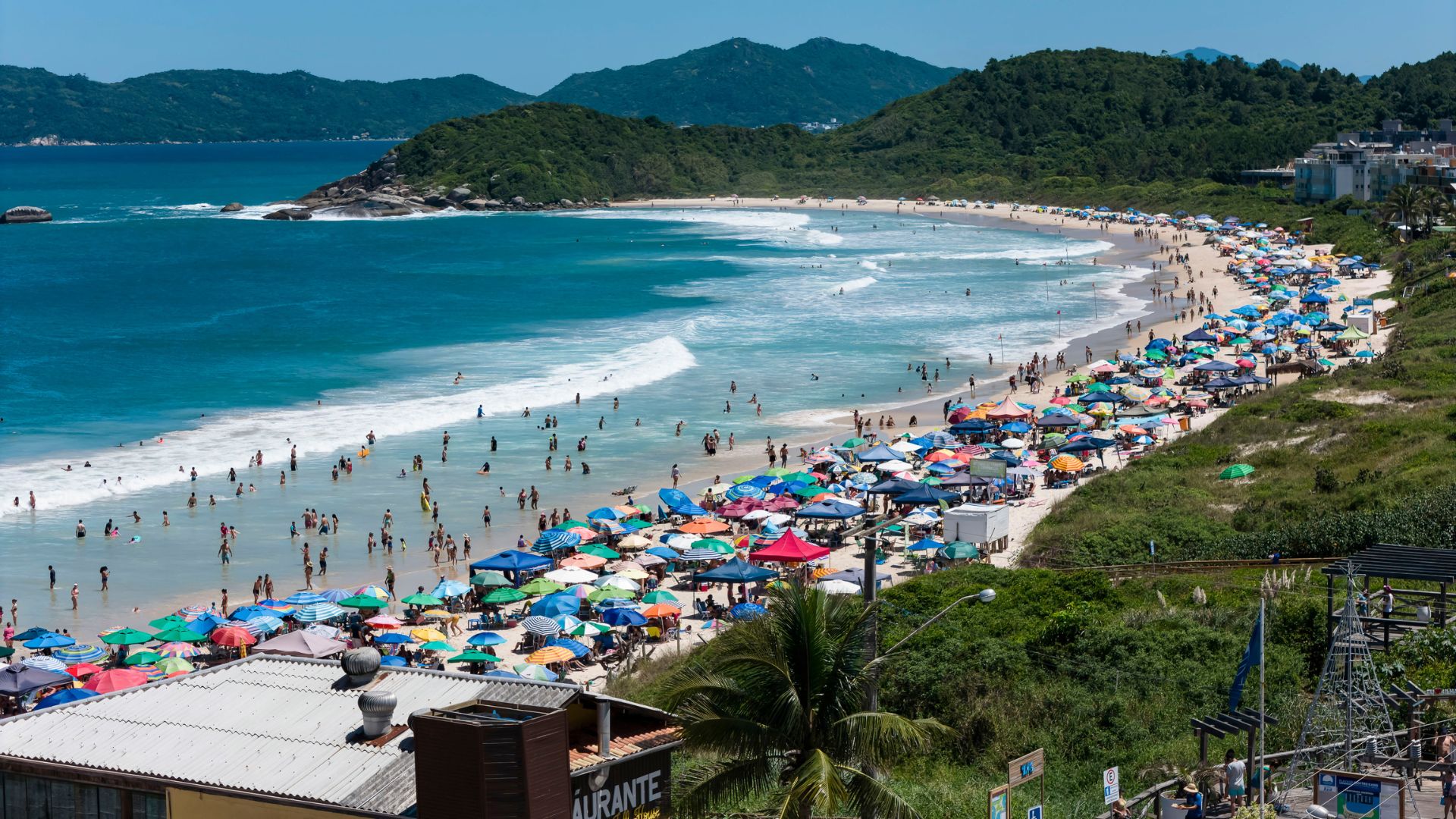 Quatro Ilhas beach in Bombinhas, Santa Catarina, with people enjoying the calm sea and practicing stand up paddle near the strip of sand - Rocccoimob Real estate in Bombinhas