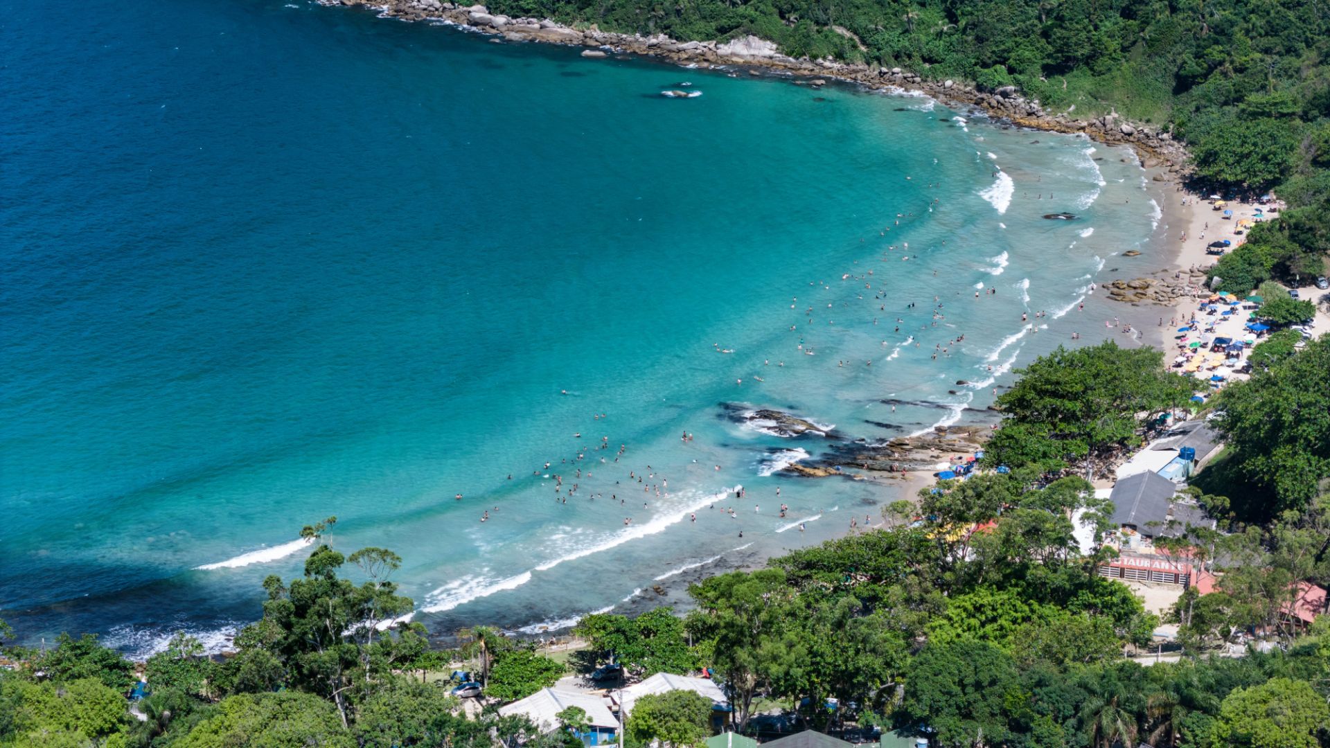 Aerial view of Retiro dos Padres Beach in Bombinhas, showing the blue sea, bathers and vegetation area around - Rocccoimob Real estate in Bombinhas