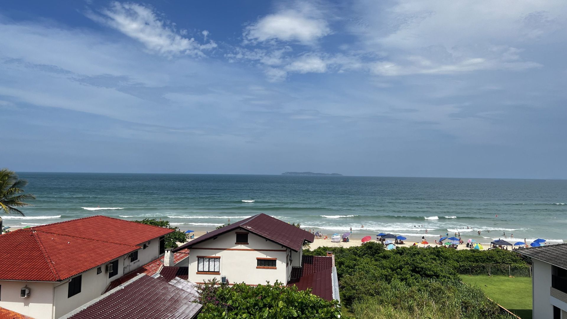 Vista de la playa de Canto Grande en Bombinhas, con mar azul, una franja de arena concurrida y casas cerca de la costa. - Inmobiliaria Rocccoimob en Bombinhas 