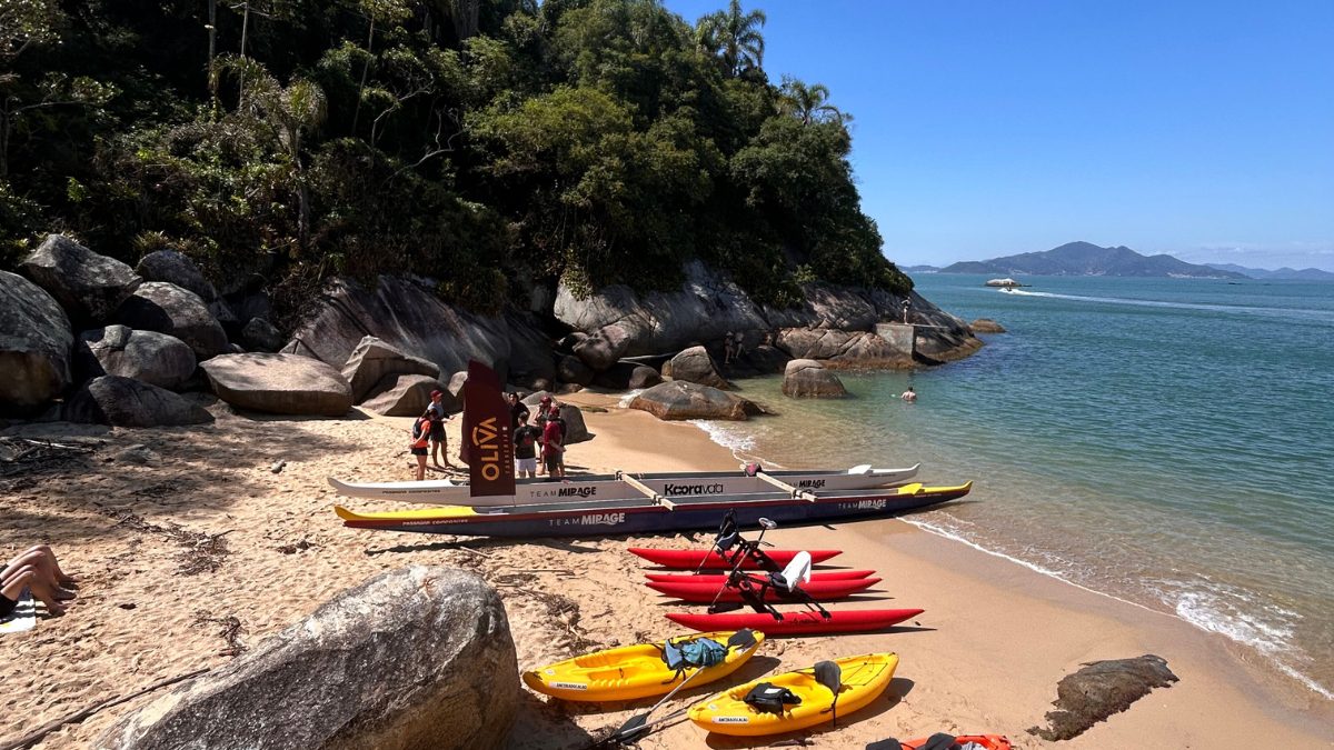 Hawaiian canoe navigating in calm waters on the coast of Bombinhas, with preserved forest and cliffs in the background - Rocccoimob Real Estate in Bombinhas