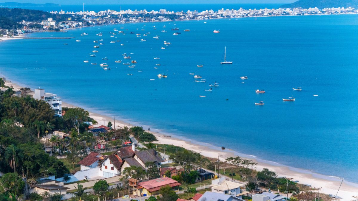 Enseada da região de Zimbros com águas calmas, barcos ancorados e orla preservada no litoral de Bombinhas - Rocccoimob Imobiliária em Bombinhas