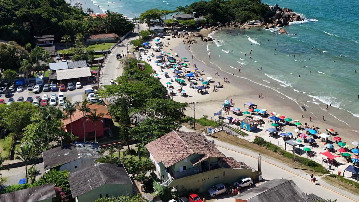 Vista aérea de la playa Mariscal en Bombinhas SC, con una franja de arena, mar azul claro, piedras naturales y zona residencial cerca del paseo marítimo - Rocccoimob Real Estate en Bombinhas
