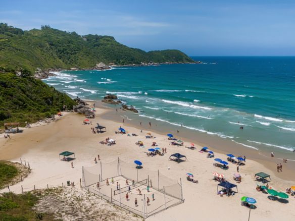 Vista aérea da Praia de Bombinhas, em Santa Catarina, com pessoas aproveitando o dia de verão - Rocccoimob Imobiliária em Bombinhas