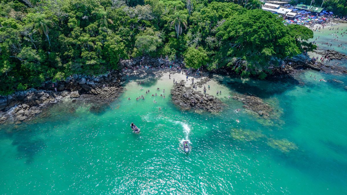 Vista aérea da Praia do Biguá em Bombinhas SC com pessoas no mar durante dia de calor - Rocccoimob Imobiliária em Bombinhas