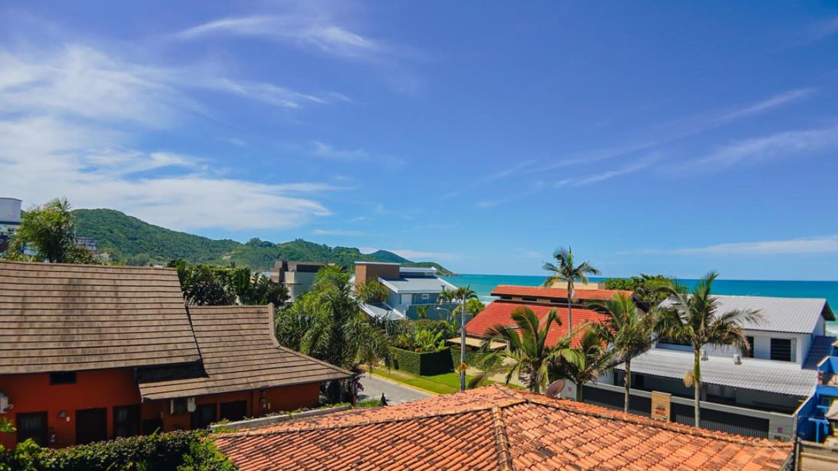 Vistas al mar en Bombinhas con casas cerca de la playa, azoteas y vegetación alrededor, en una región costera con cielos abiertos y mar de fondo - Rocccoimob Real Estate en Bombinhas