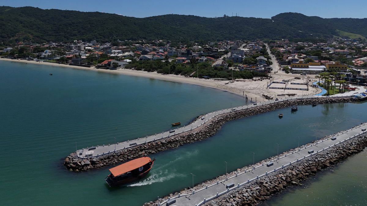 Vista aérea de Bombinhas com orla urbana e canal de acesso ao mar, evidenciando a integração entre atividades locais e o crescimento de uma economia diversificada ao longo do ano - Roccoimob Imobiliária em Bombinhas Vista aérea de Bombinhas com orla urbana e canal de acesso ao mar, evidenciando a integração entre atividades locais e o crescimento de uma economia diversificada ao longo do ano - Rocccoimob Imobiliária em Bombinhas