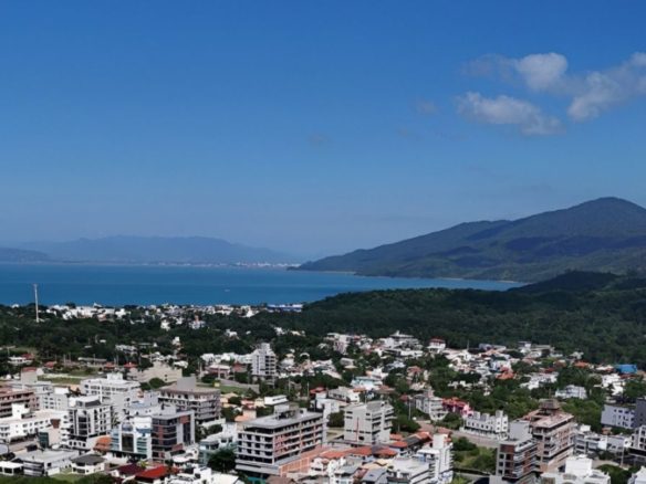 Vista aérea de Bombinhas no litoral catarinense, com área urbana consolidada entre morros e vegetação, destacando uma região com forte potencial de valorização imobiliária - Rocccoimob Imobiliária em Bombinhas