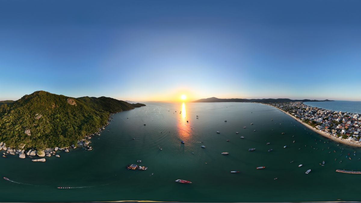 Vista aérea de cidade litorânea ao pôr do sol, mostrando as vantagens de morar no litoral com qualidade de vida - Rocccoimob Imobiliária em Bombinhas