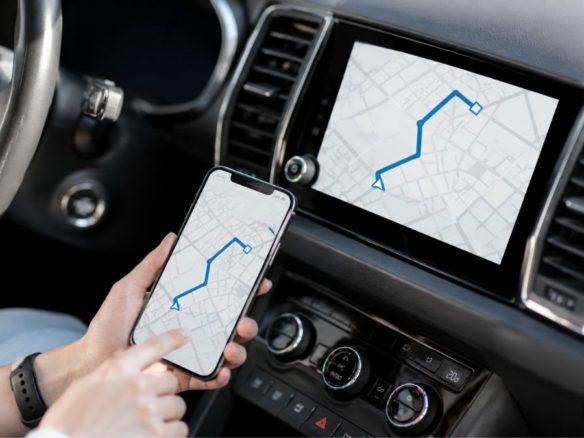 Interior de um carro moderno com smartphone exibindo aplicativo de navegação sincronizado com a central multimídia do veículo, mostrando rota em mapa digital - Rocccoimob Imobiliária em Bombinhas