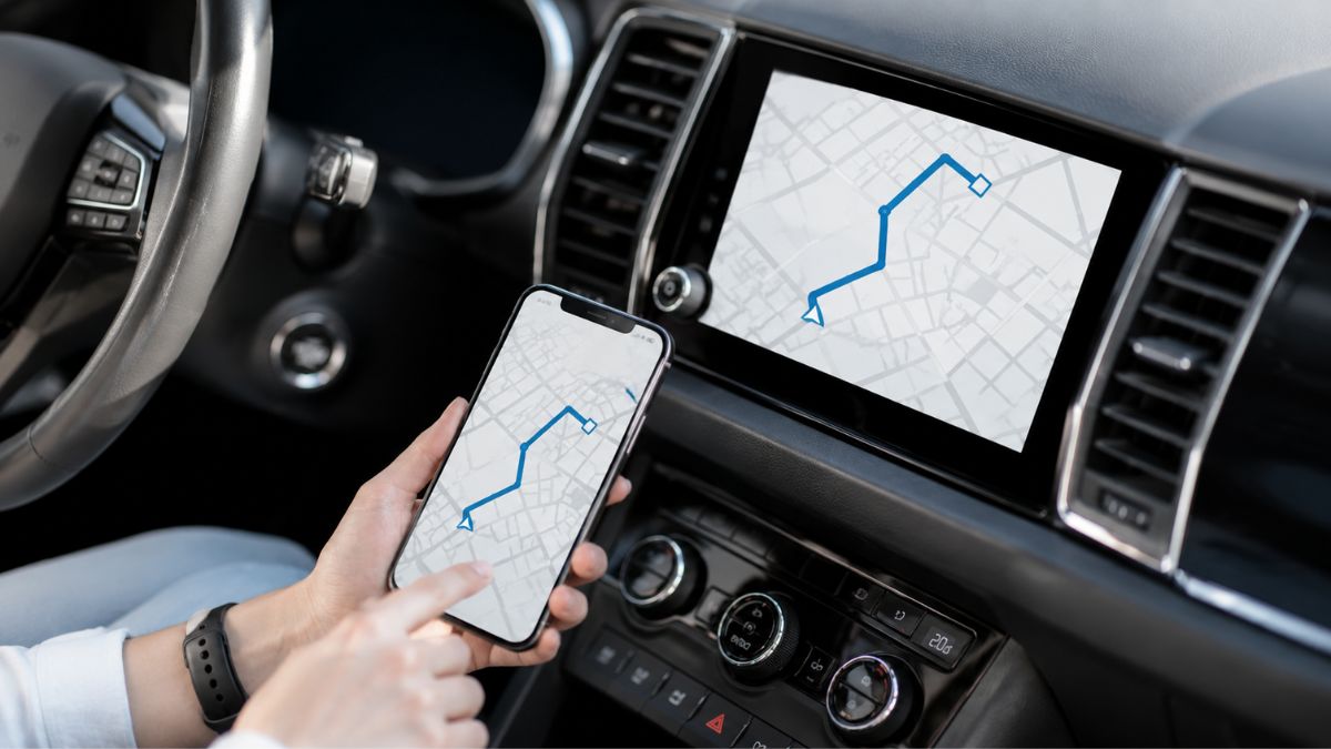 Interior de um carro moderno com smartphone exibindo aplicativo de navegação sincronizado com a central multimídia do veículo, mostrando rota em mapa digital - Rocccoimob Imobiliária em Bombinhas