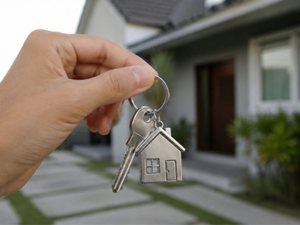 Mão segurando chave de casa em frente a um imóvel residencial, imagem relacionada ao financiamento imobiliário e compra de imóveis - Rocccoimob Imobiliária em Bombinhas