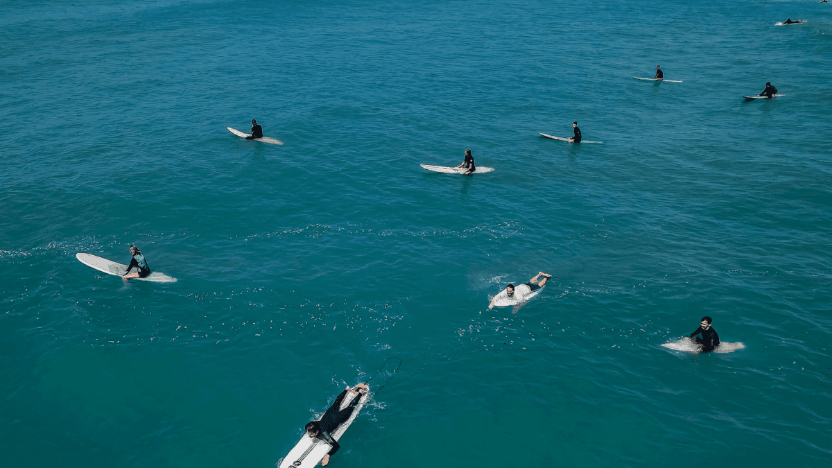 Surfistas com pranchas no mar azul de Bombinhas em Santa Catarina, prática de surf e esportes náuticos na região - Rocccoimob Imobiliária em Bombinhas