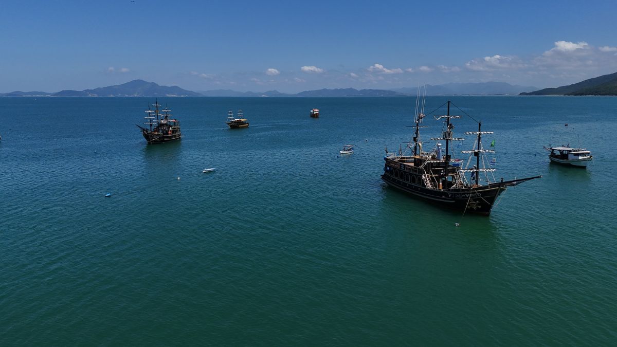 Bombinhas, cidade onde acontece a Rota da Tainha, com barcos no mar e vista panorâmica do litoral - Rocccoimob Imobiliária em Bombinhas